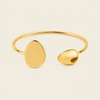 A polished gold open cuff bracelet with two organic, rounded disc-like ends, photographed on a clean, solid off-white background.