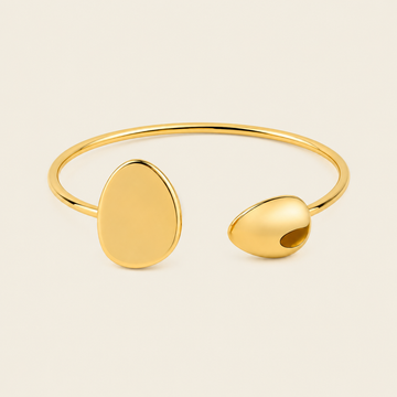 A polished gold open cuff bracelet with two organic, rounded disc-like ends, photographed on a clean, solid off-white background.