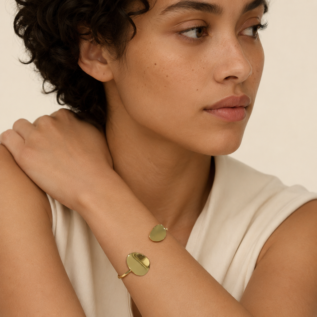 Woman wearing gold bracelets on a neutral background