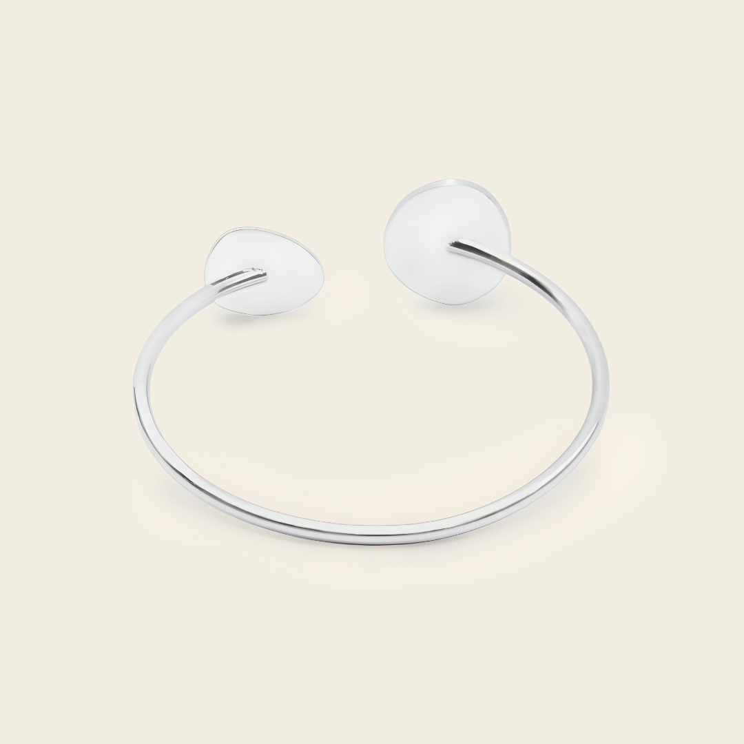 A minimalist silver-toned open cuff bangle bracelet with smooth, rounded disc-like ends, displayed on a solid light beige background.