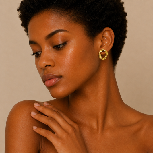 A close-up of a woman with short dark hair wearing a textured gold hoop earring, set against a warm beige background.