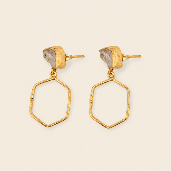 Gold earrings with geometric designs on a beige background