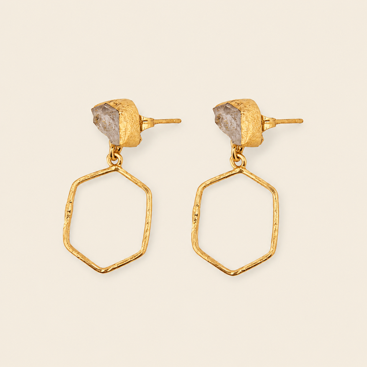 Gold earrings with geometric designs on a beige background