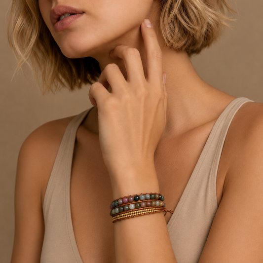 Woman wearing a beige top and multiple bracelets on her wrist against a neutral background