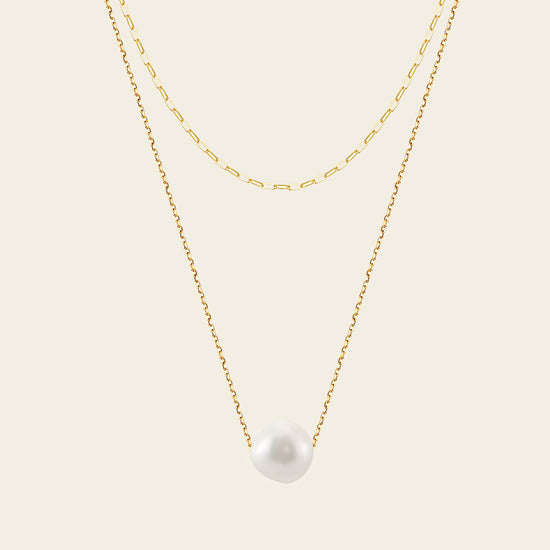 Two gold necklaces with a pearl pendant on a beige background
