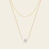 Two gold necklaces with a pearl pendant on a beige background