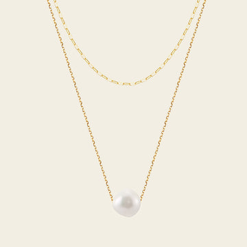 Two gold necklaces with a pearl pendant on a beige background