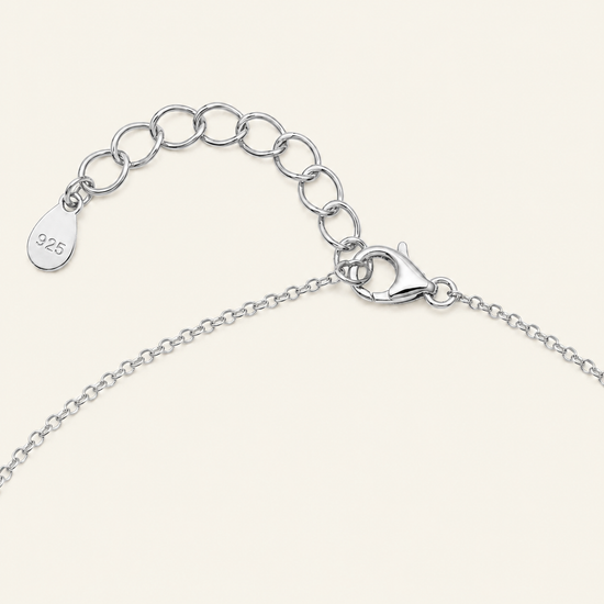 Close-up of a silver chain necklace showing an adjustable lobster clasp, extension chain with oval links, and a small teardrop tag stamped with '925' on a light cream background.
