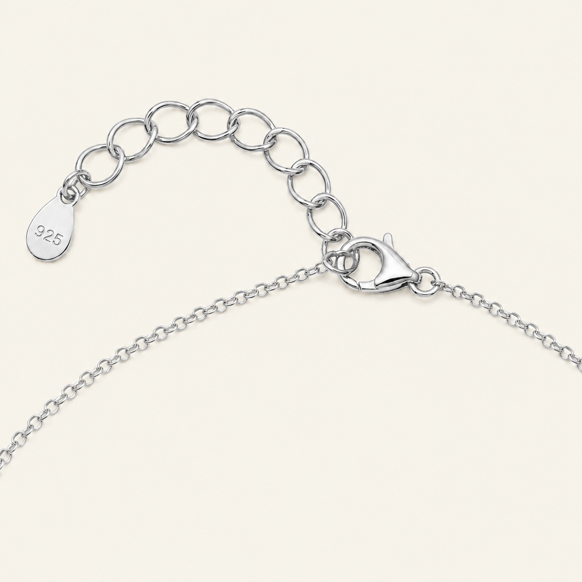 Close-up of a silver chain necklace showing an adjustable lobster clasp, extension chain with oval links, and a small teardrop tag stamped with '925' on a light cream background.