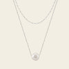 Pearl necklace on a thin chain against a light background