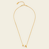 A delicate gold chain necklace featuring a small white pearl and two small gold disc charms, displayed on a light cream background.