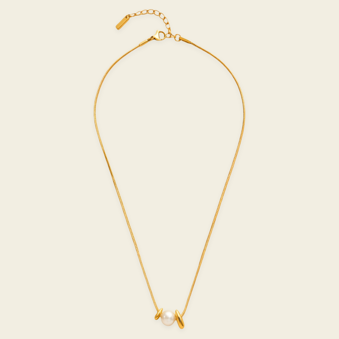 A delicate gold chain necklace featuring a small white pearl and two small gold disc charms, displayed on a light cream background.