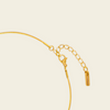 Close-up of a gold chain necklace with a lobster clasp, extension chain, and a small rectangular tag on a light cream background.