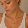 Woman wearing a gold necklace with a pearl pendant against a neutral background