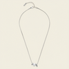 A delicate gold chain necklace featuring a small white pearl and two small gold disc charms, displayed on a light cream background.