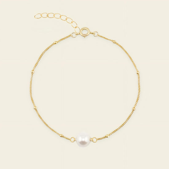 Gold bracelet with a single pearl on a beige background