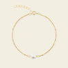 Gold bracelet with a single pearl on a beige background