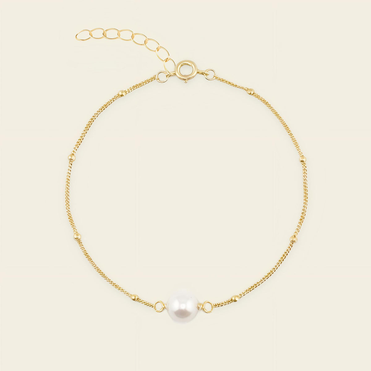 Gold bracelet with a single pearl on a beige background