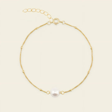 Gold bracelet with a single pearl on a beige background