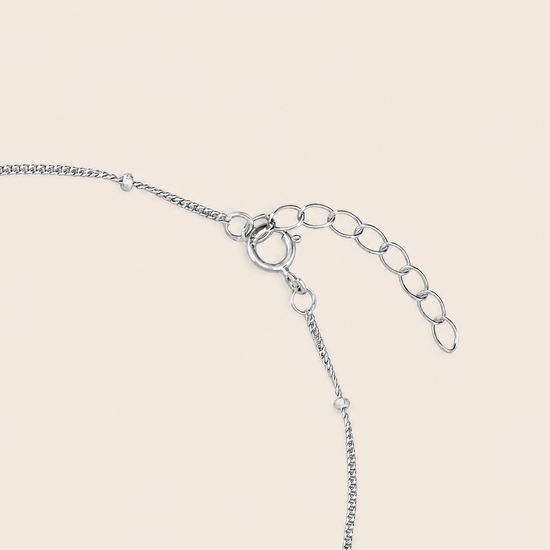 Silver chain extender with a lobster clasp and oval link chain on a light beige background.