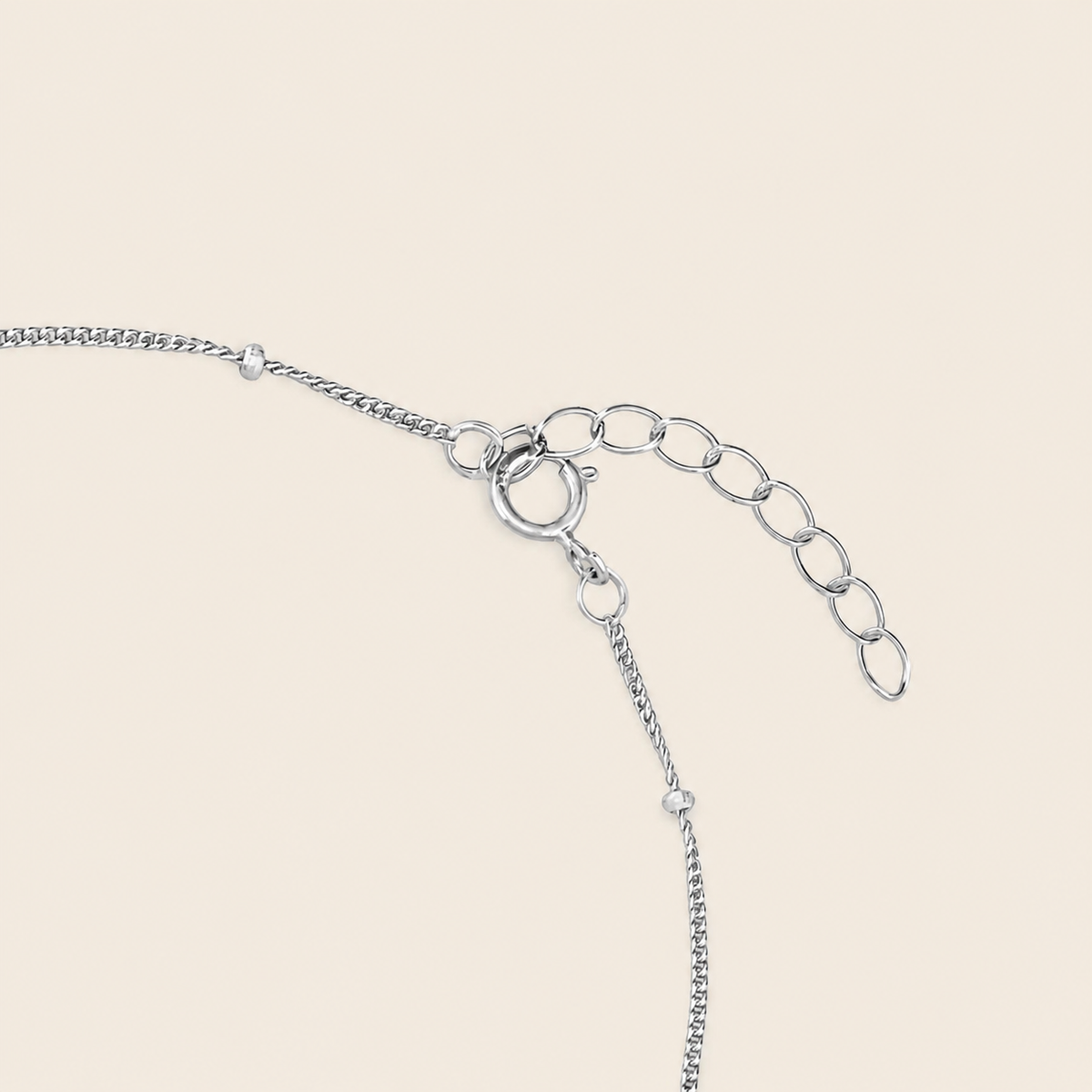 Silver chain extender with a lobster clasp and oval link chain on a light beige background.