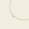 Gold necklace with a single pearl on a beige background
