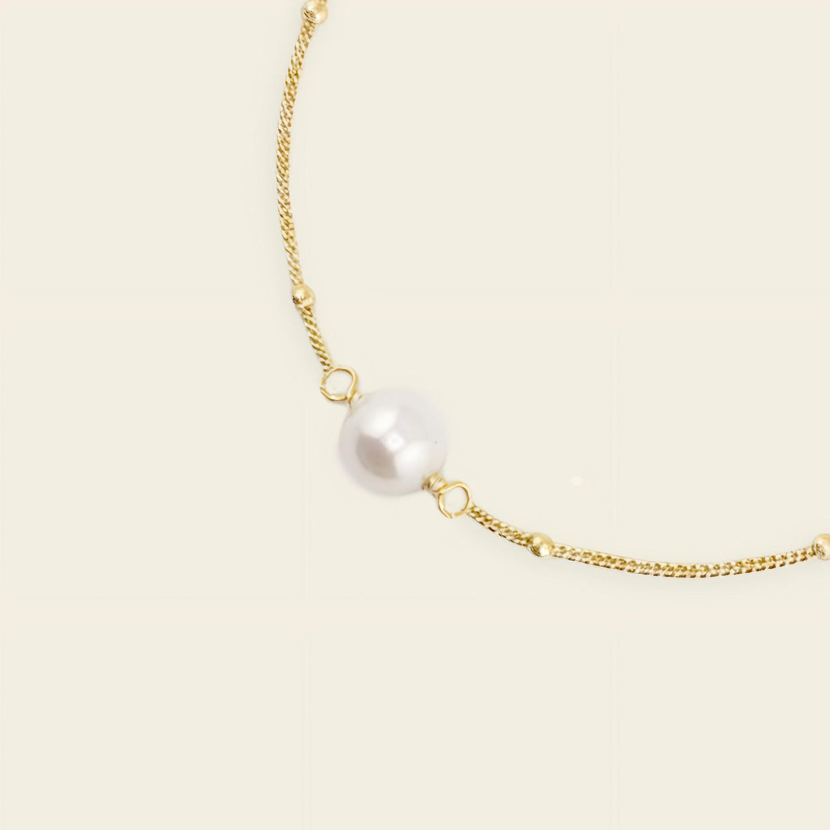 Gold necklace with a single pearl on a beige background