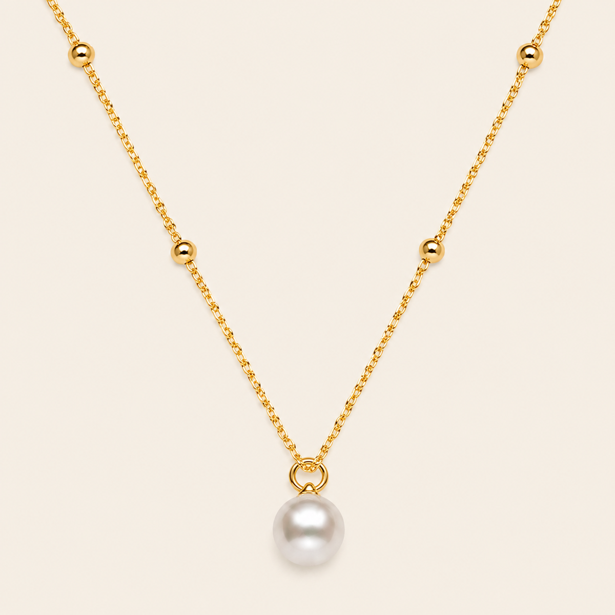 Gold necklace with a single pearl pendant on a beige background