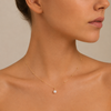 Close-up of a woman wearing a delicate gold necklace with a pearl pendant on a neutral background