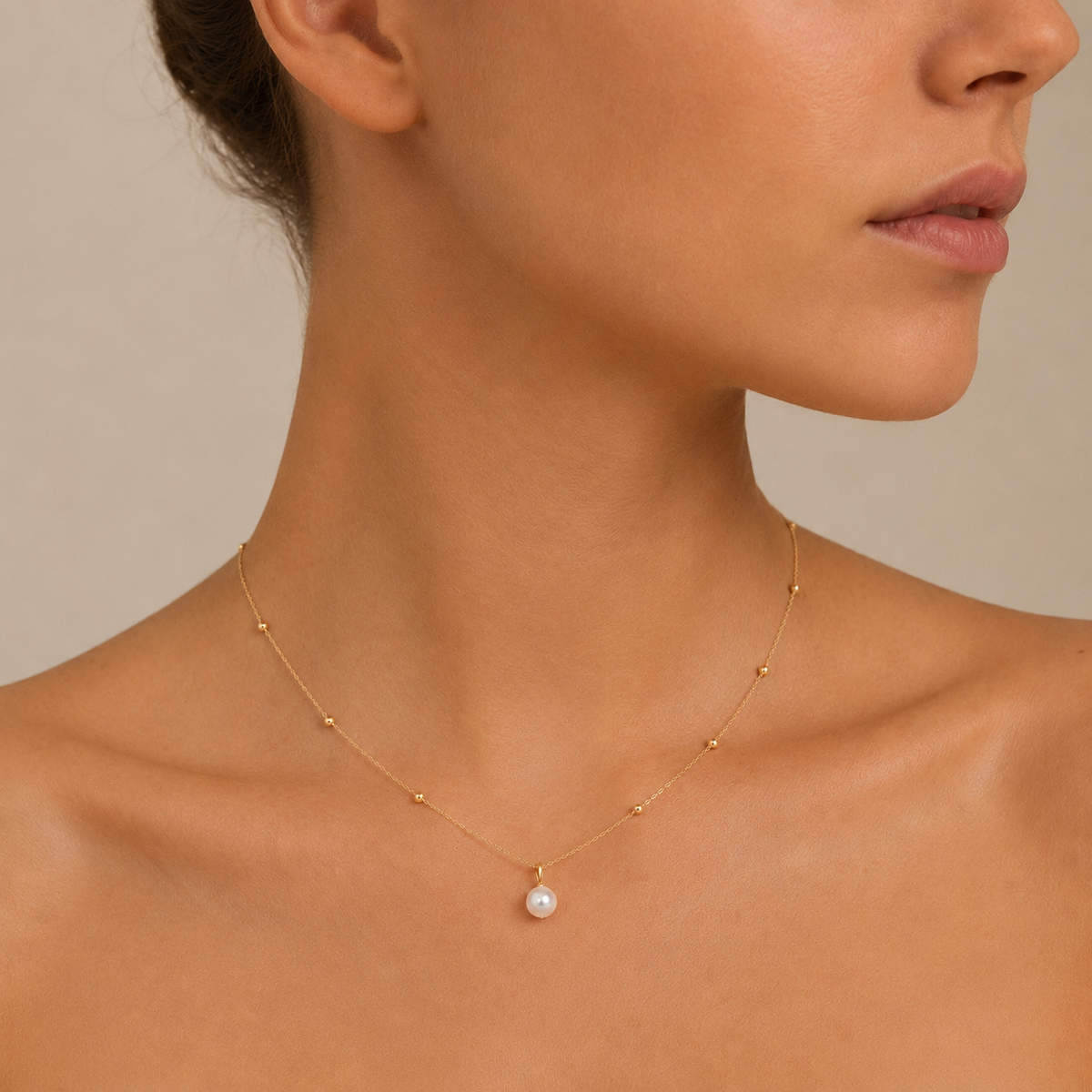 Close-up of a woman wearing a delicate gold necklace with a pearl pendant on a neutral background