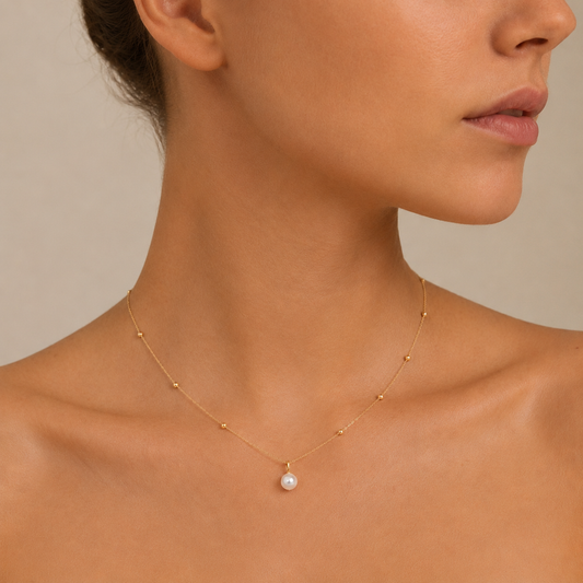 Close-up of a woman wearing a delicate gold necklace with a pearl pendant on a neutral background
