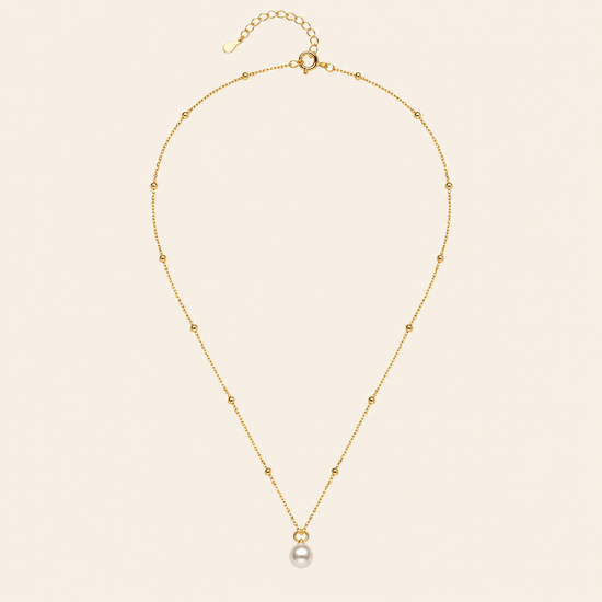 Gold necklace with a single pearl pendant on a beige background