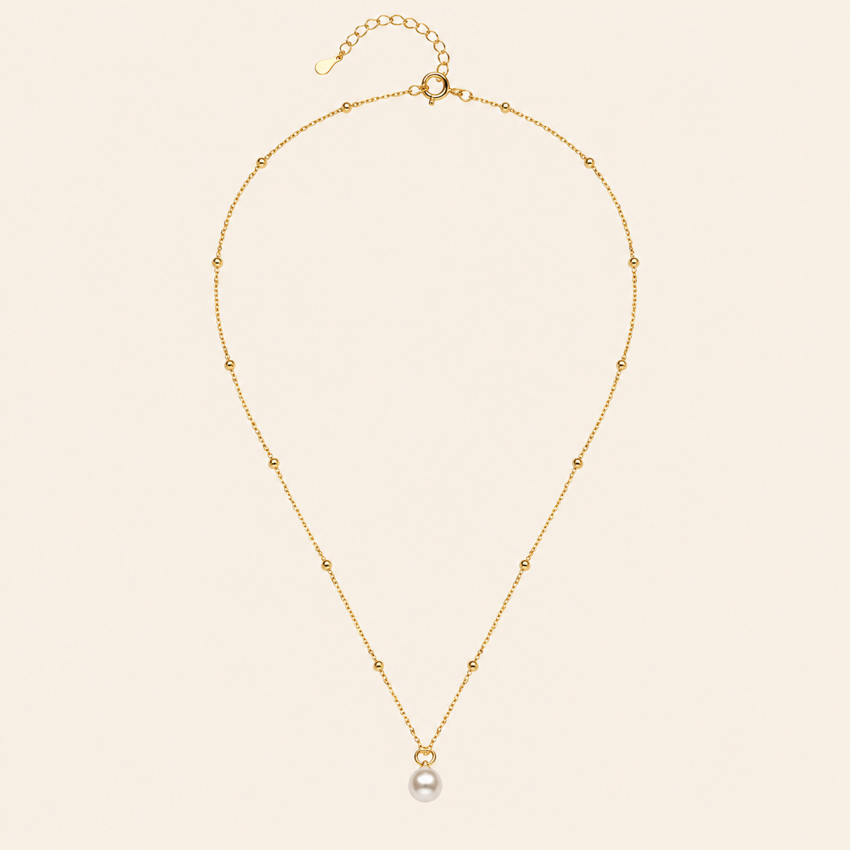 Gold necklace with a single pearl pendant on a beige background