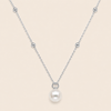 A delicate silver chain necklace featuring a single white pearl pendant suspended from a small silver ring, accented with small silver beads along the chain, set against a solid pale beige background.