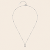 A delicate silver chain necklace featuring a single white pearl pendant, accented with small sparkling beads spaced along the chain, displayed against a solid pale beige background.