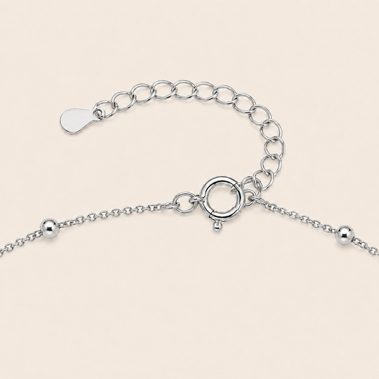 Silver chain bracelet extension with a lobster clasp, ring extender, and small bead details on a light beige background.