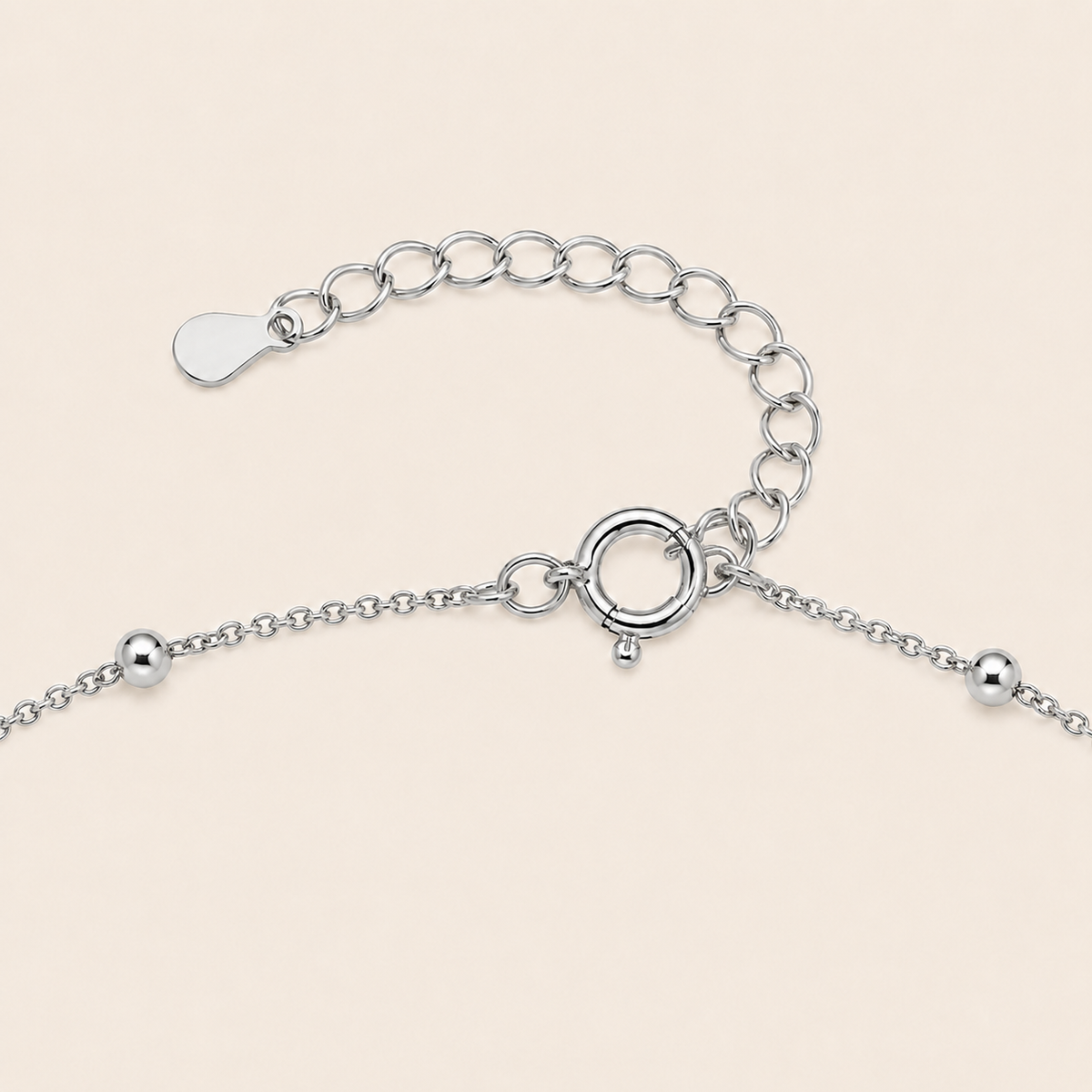 Silver chain bracelet extension with a lobster clasp, ring extender, and small bead details on a light beige background.