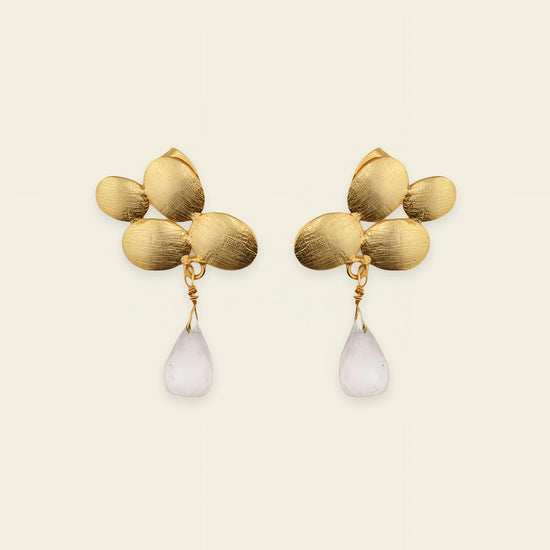 Gold earrings with leaf-like designs and white teardrop-shaped stones on a beige background