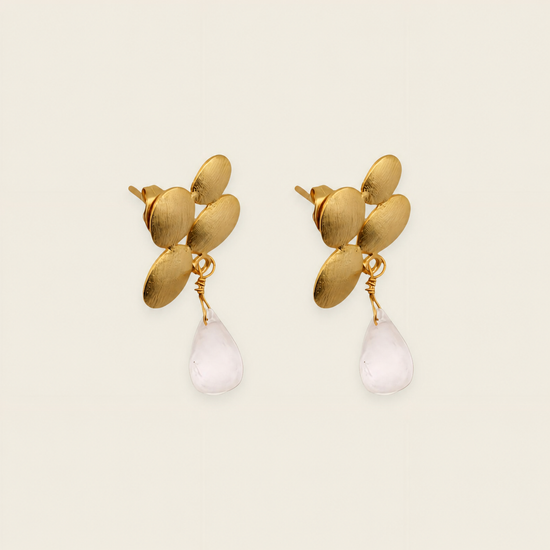 Gold earrings with leaf-like designs and white teardrop-shaped stones on a beige background
