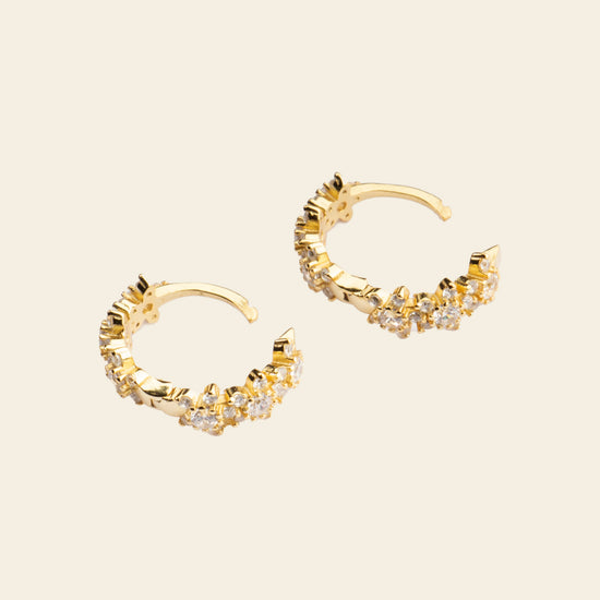Gold hoop earrings with diamond accents on a beige background