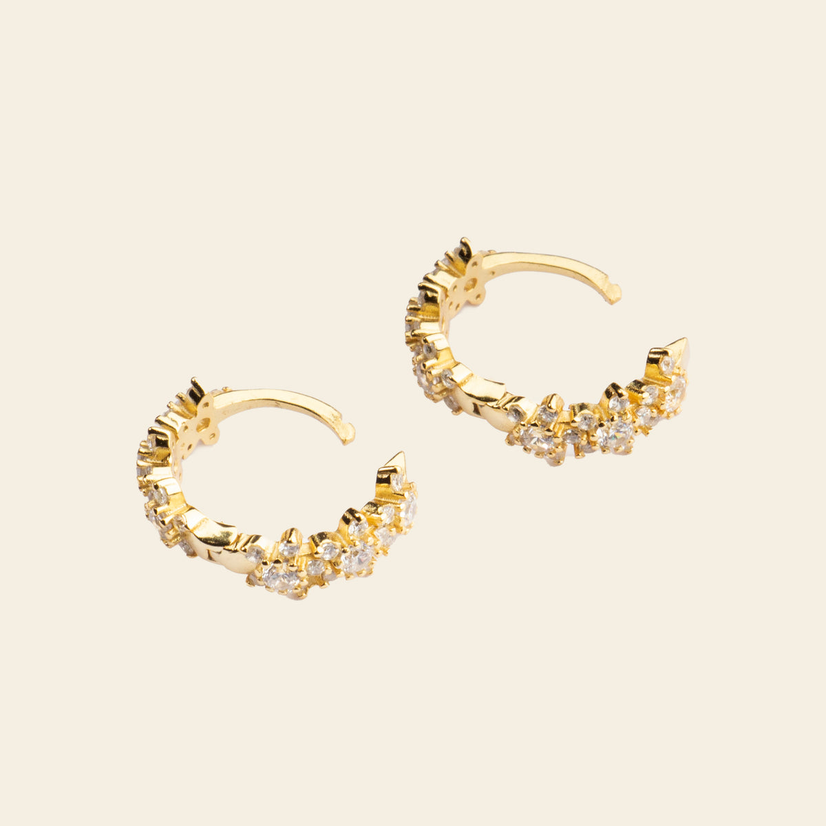 Gold hoop earrings with diamond accents on a beige background