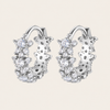Pair of silver hoop earrings with clear gemstones on a light beige background