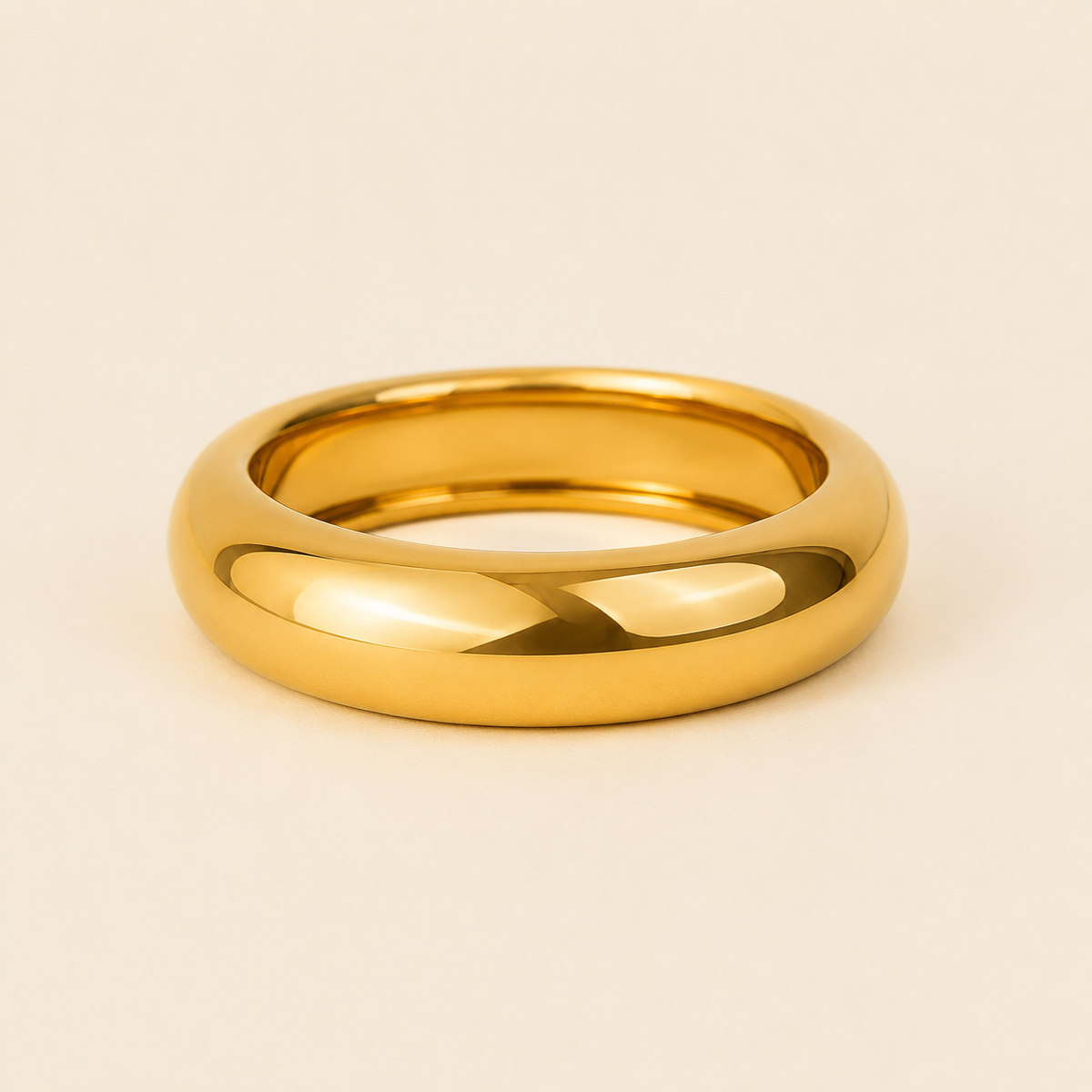 A polished yellow gold band ring with a smooth, rounded profile, photographed on a clean, solid, warm off-white background.