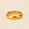 A polished yellow gold band ring with a smooth, rounded profile, photographed on a clean, solid, warm beige background.