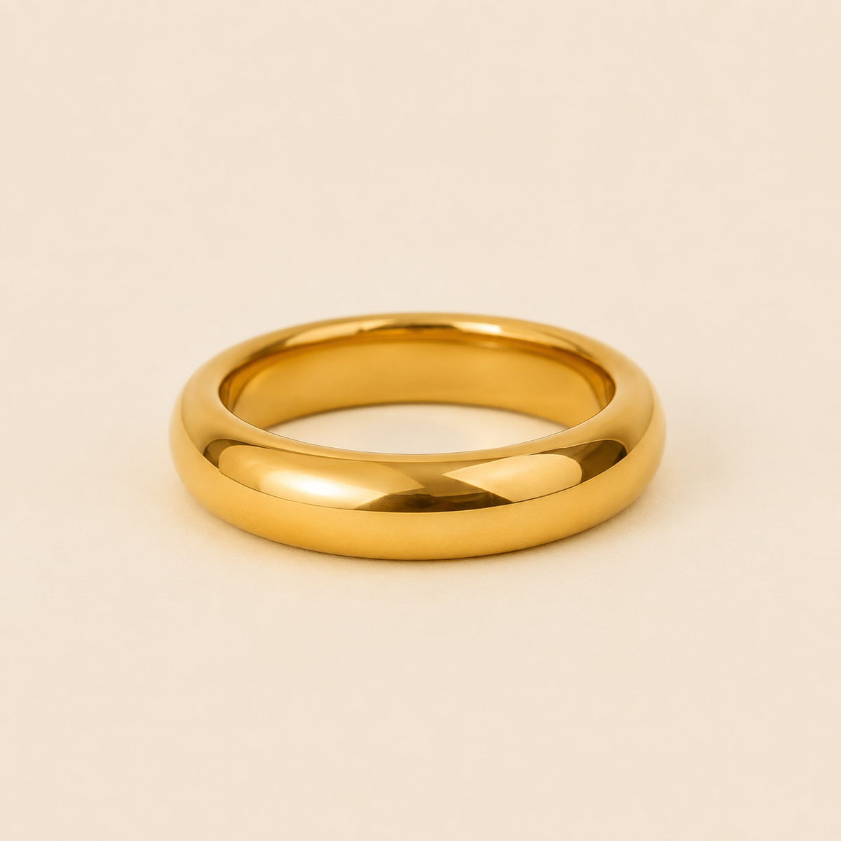 A polished yellow gold band ring with a smooth, rounded profile, photographed on a clean, solid, warm beige background.