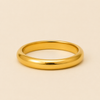 A polished yellow gold band ring with a smooth, rounded profile, displayed on a solid light beige background.