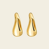 A pair of abstract, teardrop-shaped gold earrings with a polished, reflective finish, displayed on a solid light beige background.