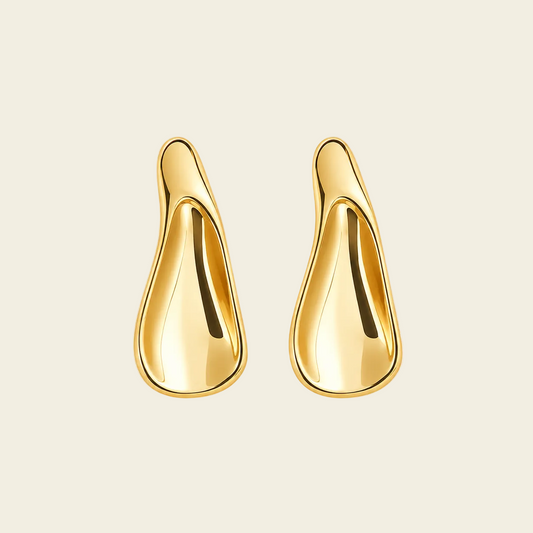 A pair of abstract, teardrop-shaped gold earrings with a polished, reflective finish, displayed on a solid light beige background.