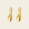 A pair of polished gold abstract teardrop-shaped stud earrings on a light cream background.