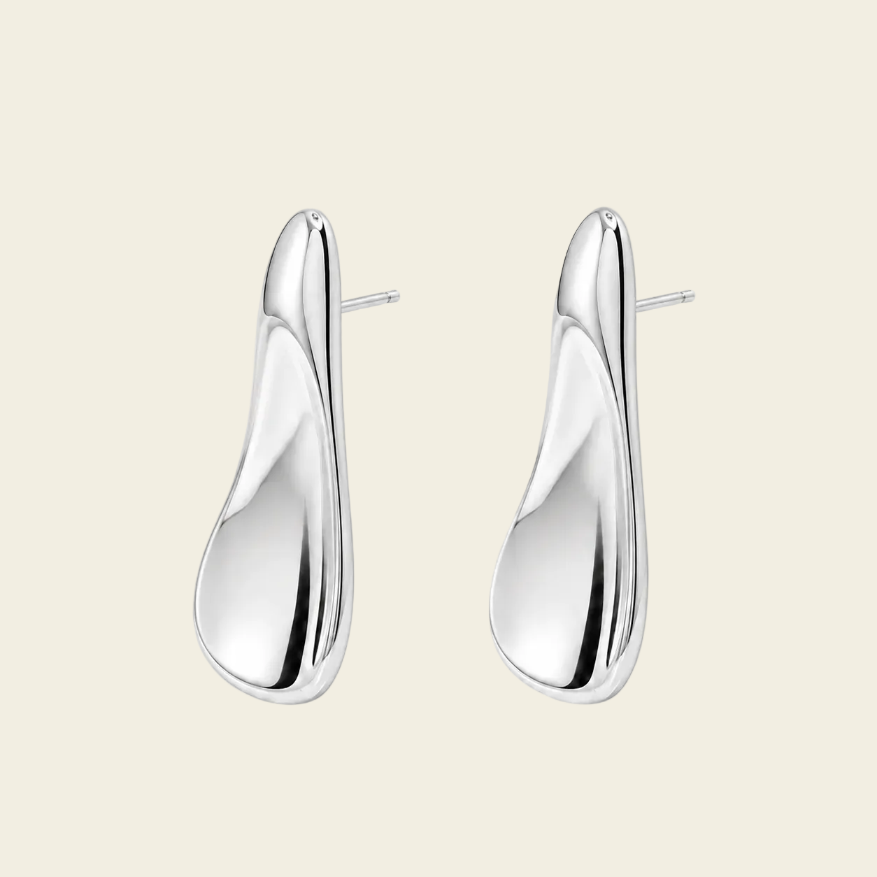 A pair of polished silver drop earrings with a smooth, organic teardrop shape and post backs, displayed on a solid light beige background.